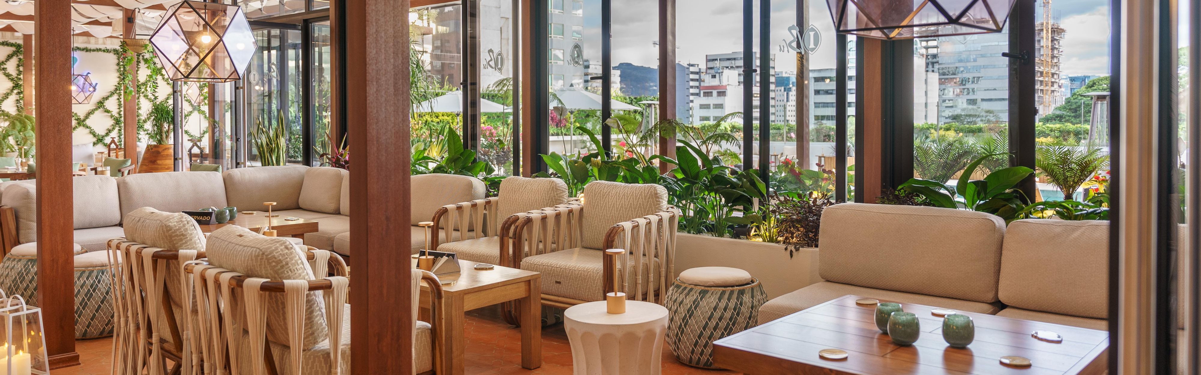 Salón interior y exterior con mesas, sillas tejidas y exuberantes vistas