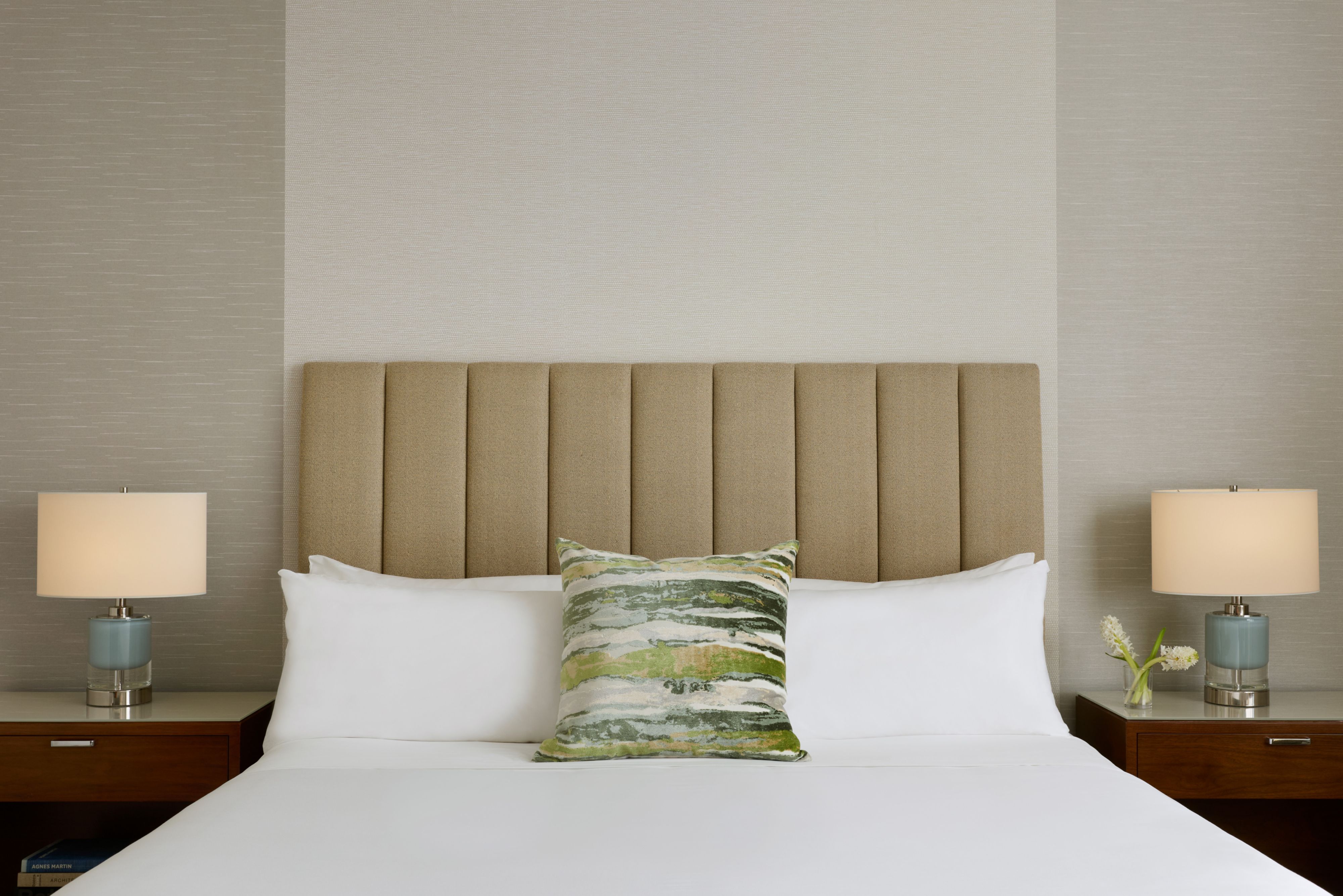 Guest room with a white bed, upholstered headboard, decorative accent pillow, and matching bedside lamps.