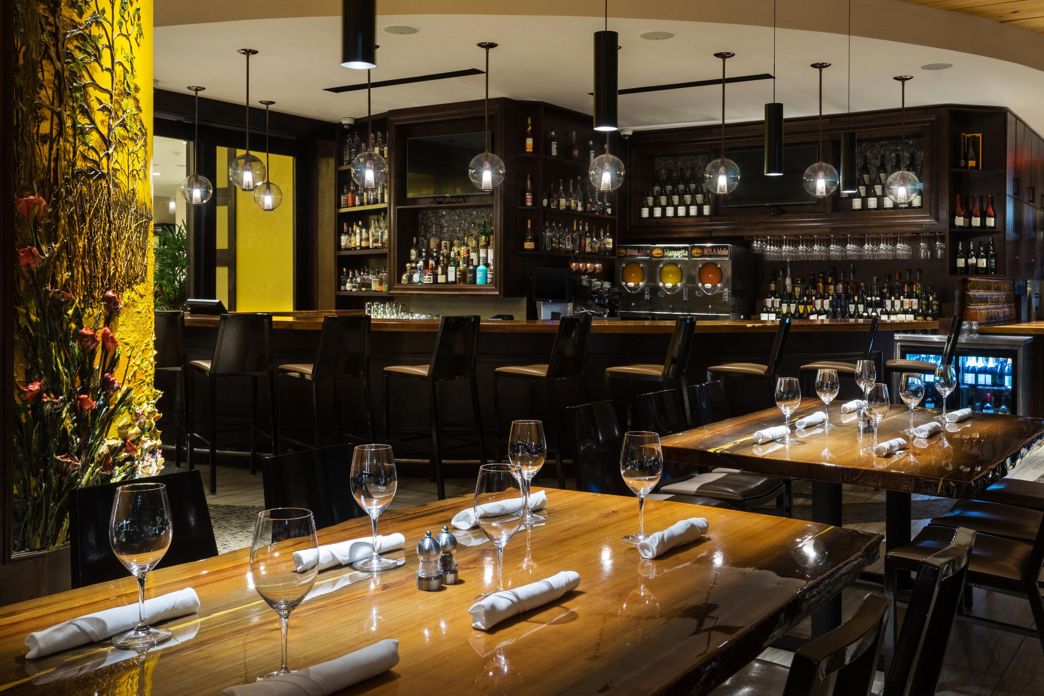 Upscale restaurant dining room with wood tables, bar seating, and pendant lighting
