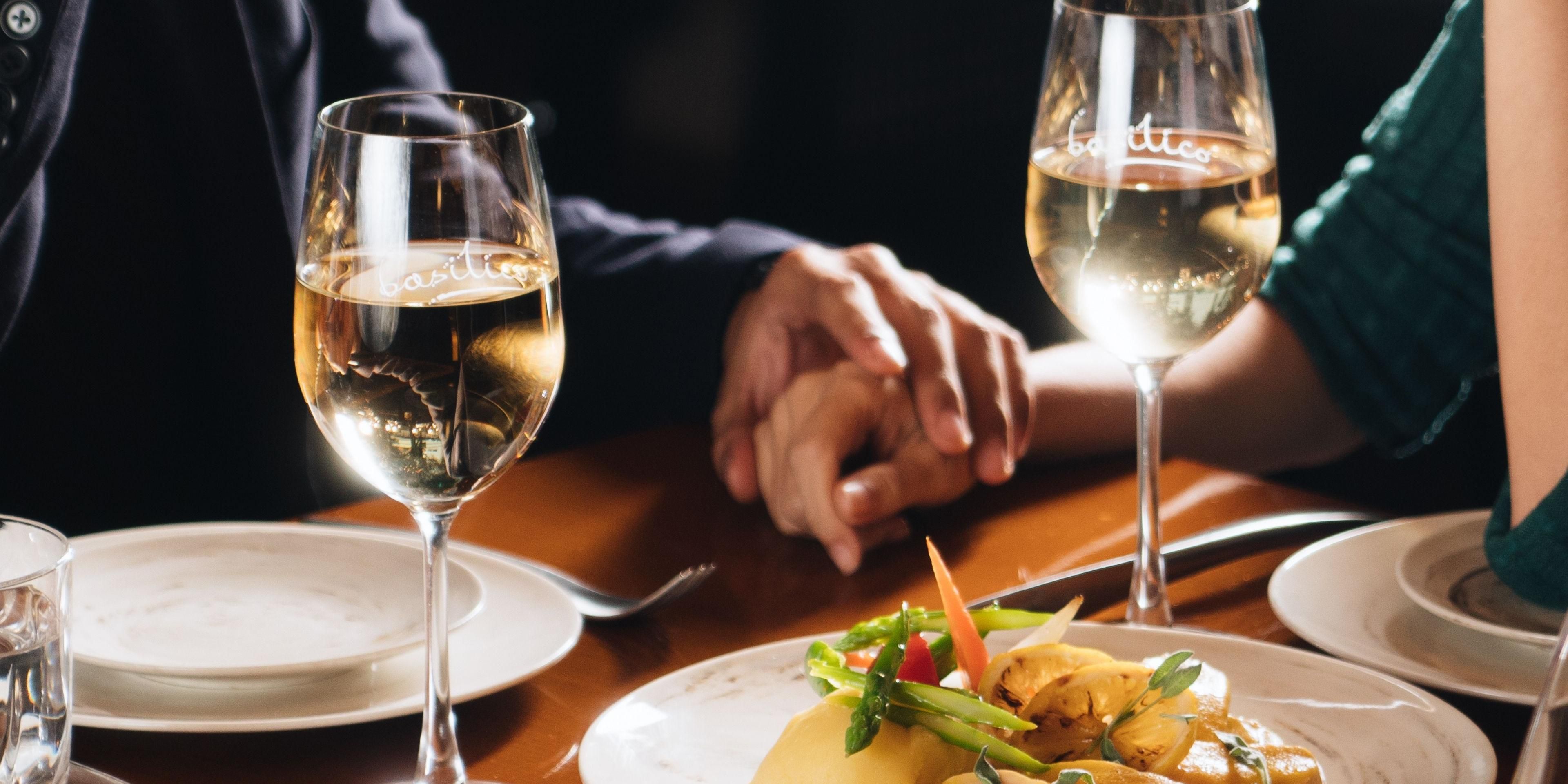 Couple holding hands over dinner table with wine glasses and plated meal