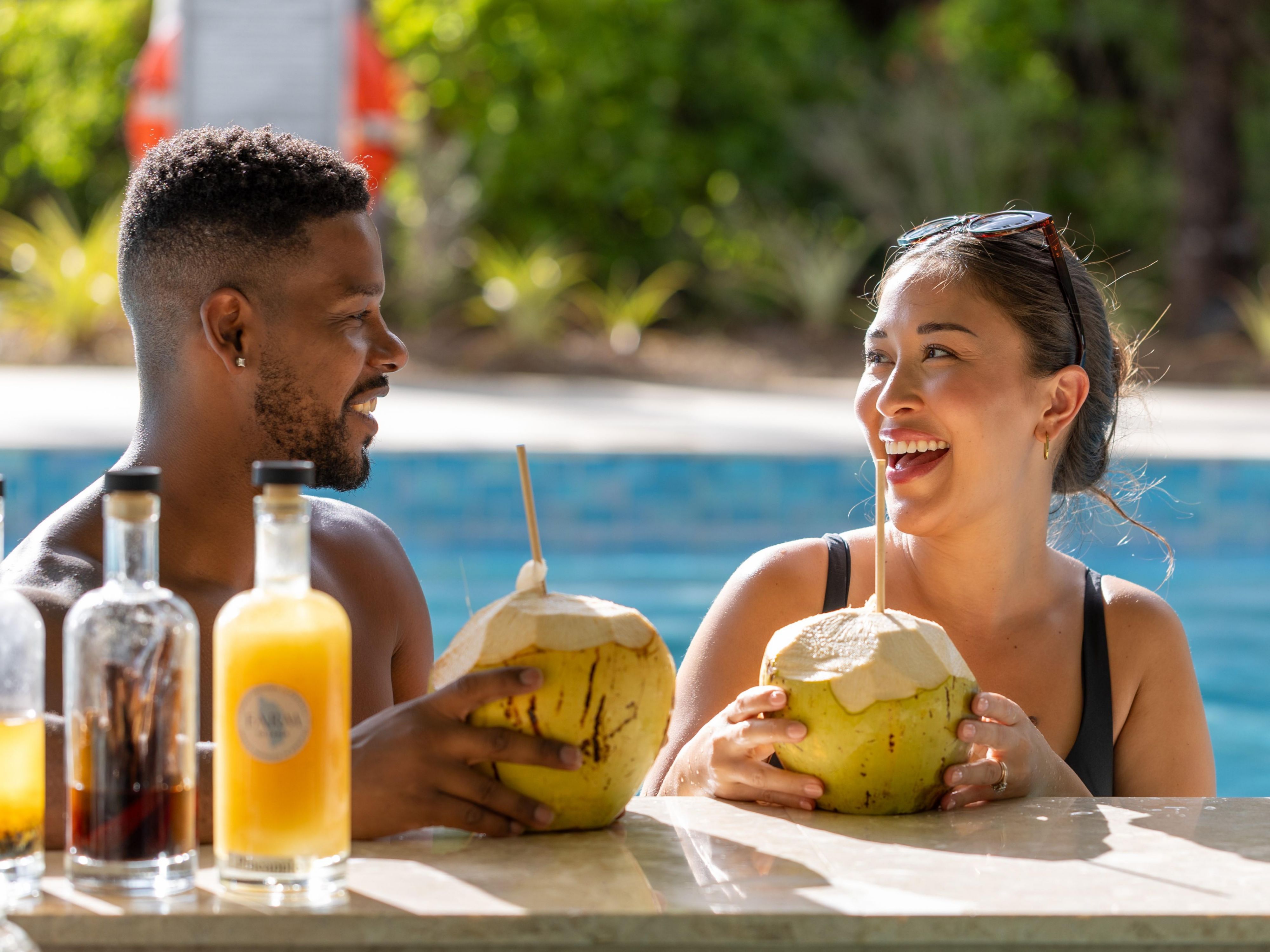 Couple enjoying water from fresh coconuts by the pool.