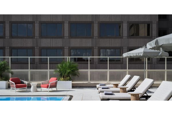 Outdoor pool deck with lounge chairs, shaded seating, and modern hotel architecture in the background.