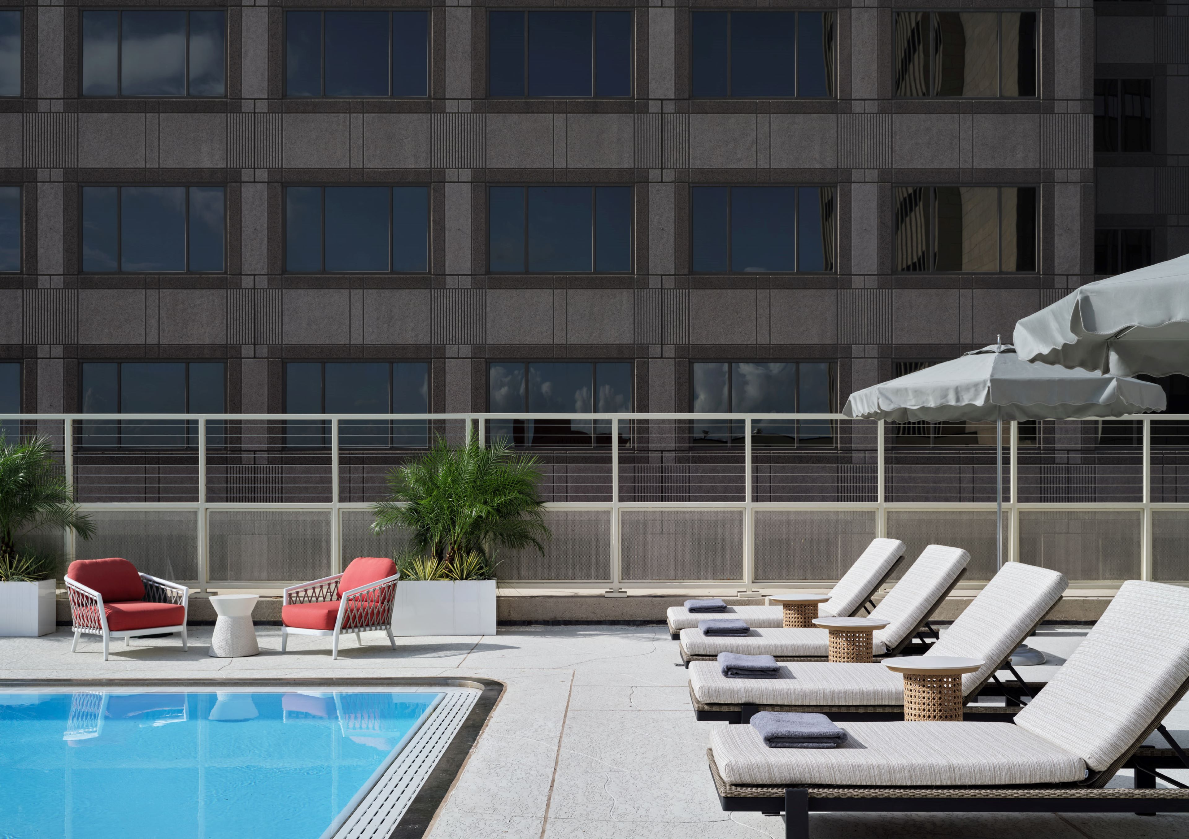 Poolside deck with lounge chairs and umbrellas beside a modern building.