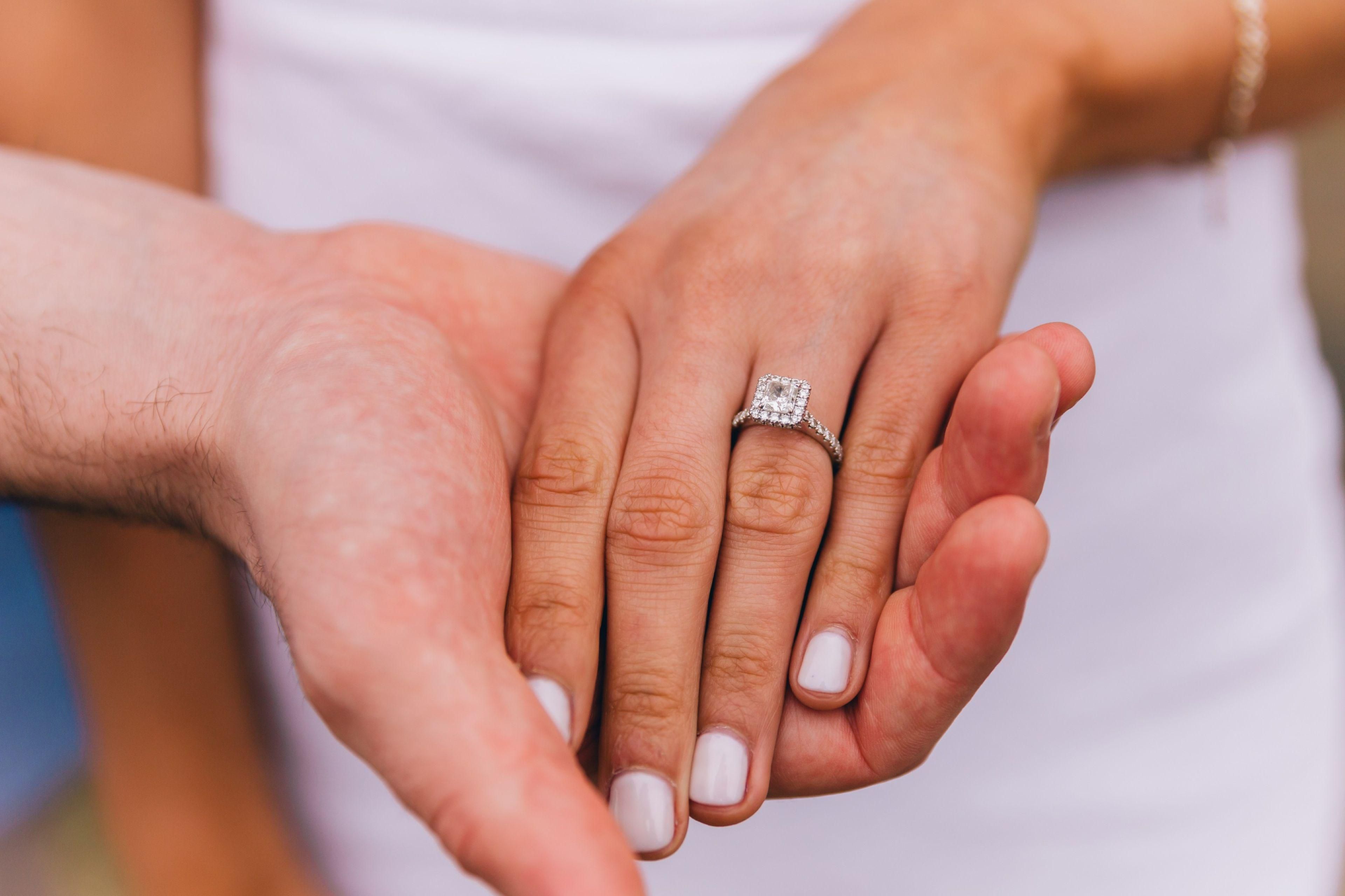 Close-up of an engagement ring on intertwined hands.