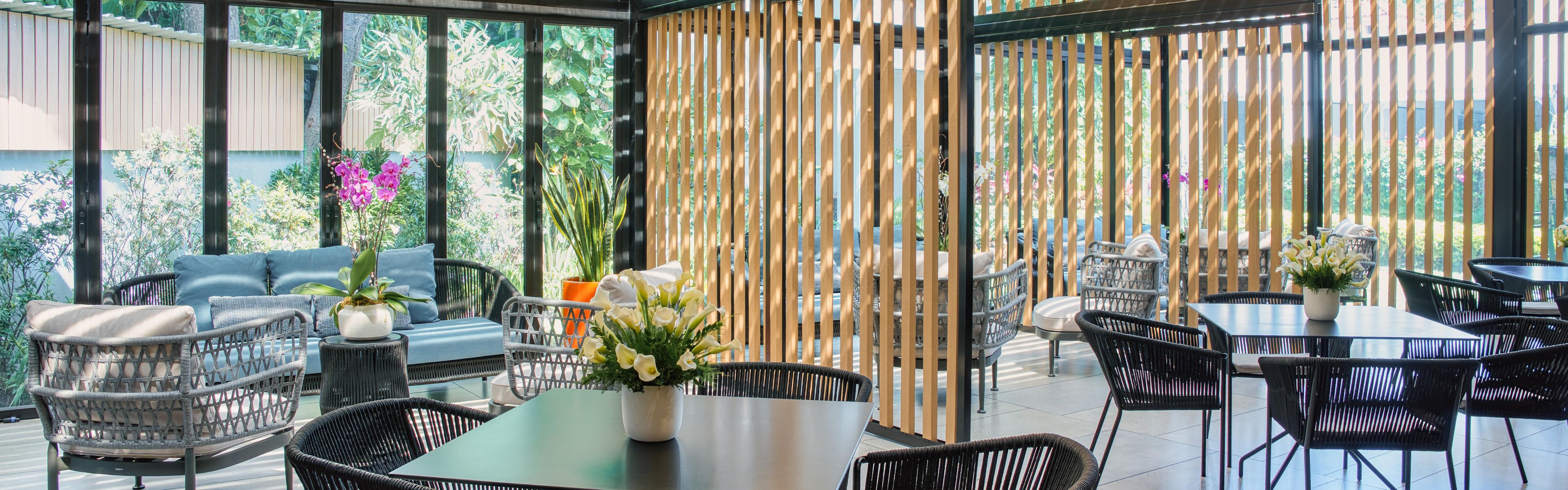 Indoor-outdoor lounge with tables, woven chairs, and lush views