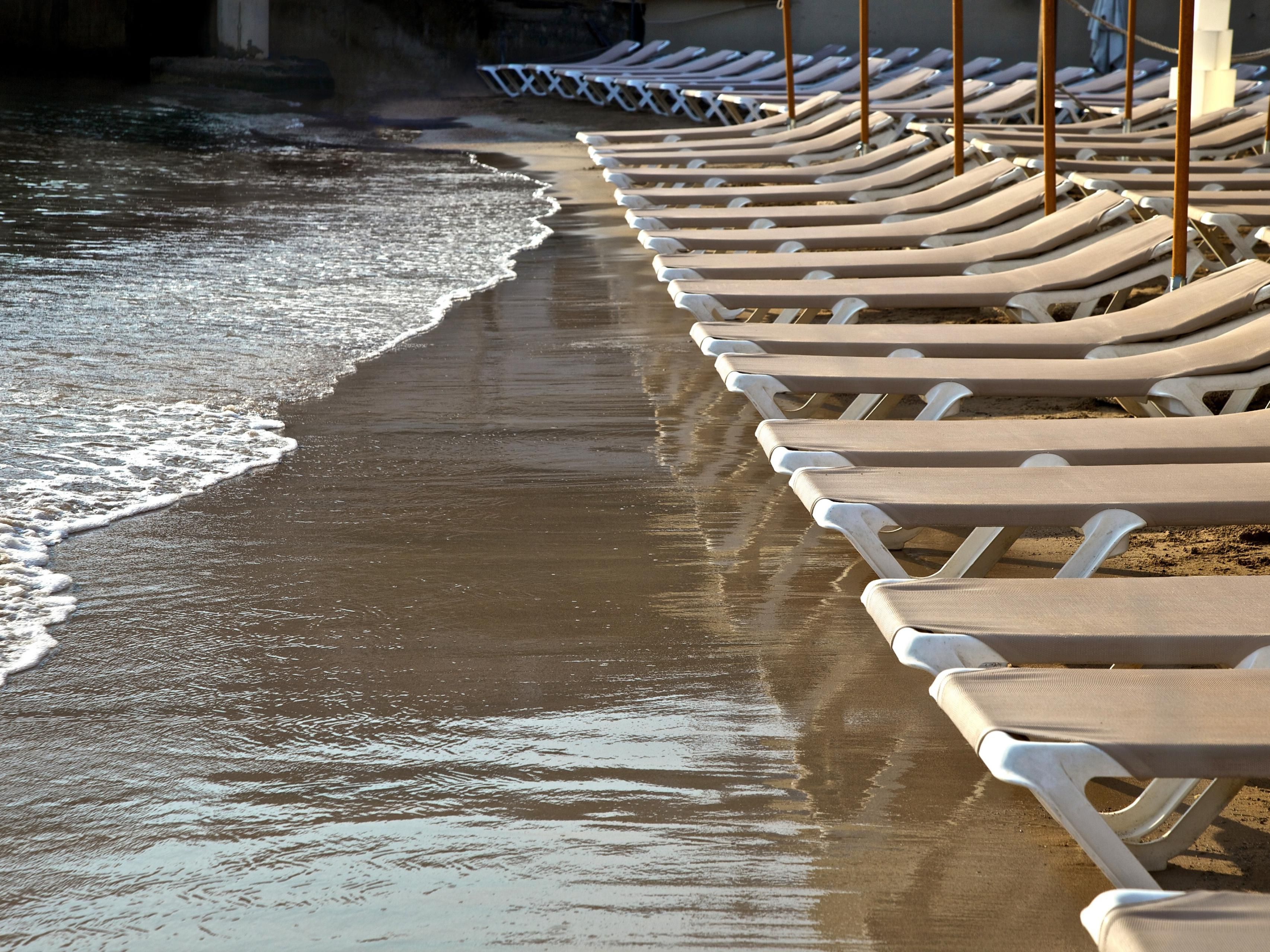 Row of empty lounge chairs lined up along a sandy beach shoreline
