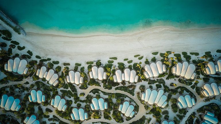 Bright hotel room with a wooden slat divider, small table and chairs, and a desk by a window. 