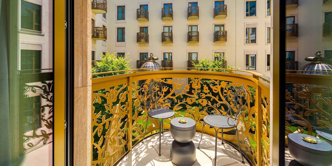 A hotel balcony with and ornate railing and cozy seating for two people.
