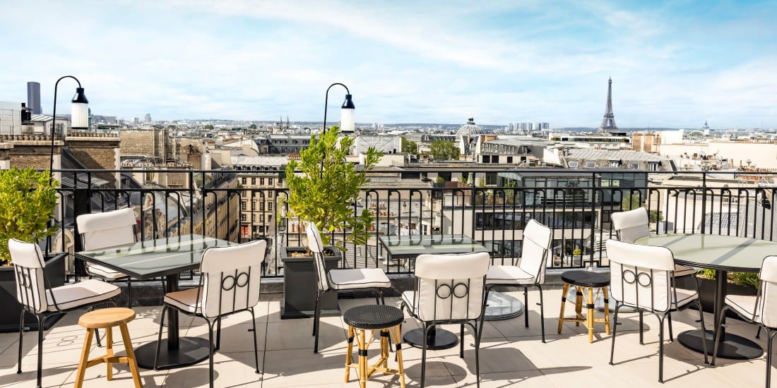 A roof top cafe overlooking the city with comfortable dining tables and chairs.