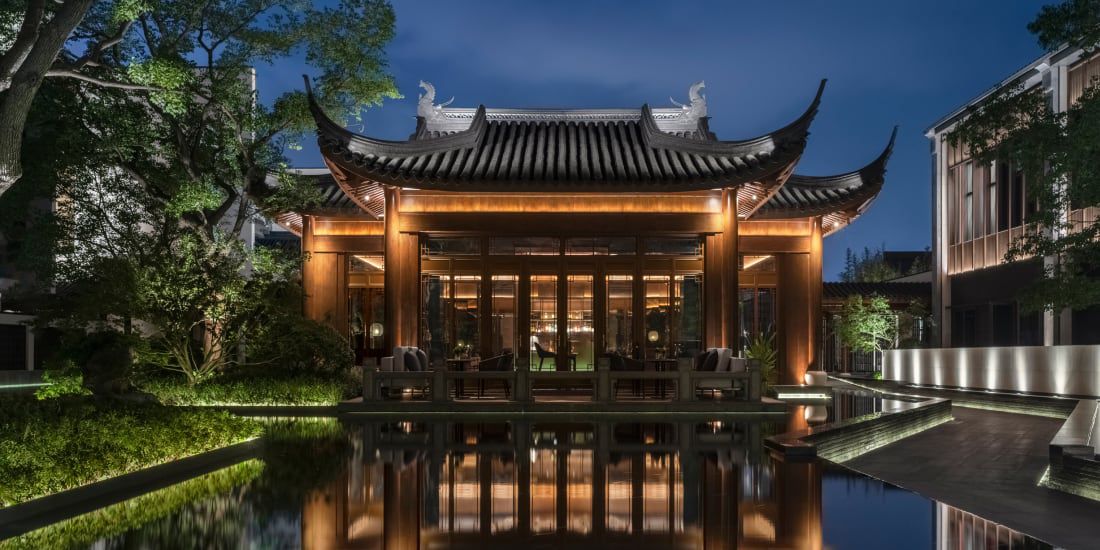 A hotel with a pagoda roof overlooking a reflecting pool at night.