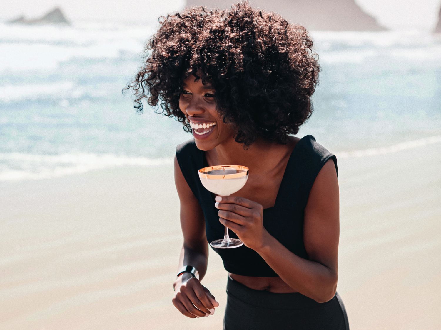 A woman walking on the beach with a drink in her hand.