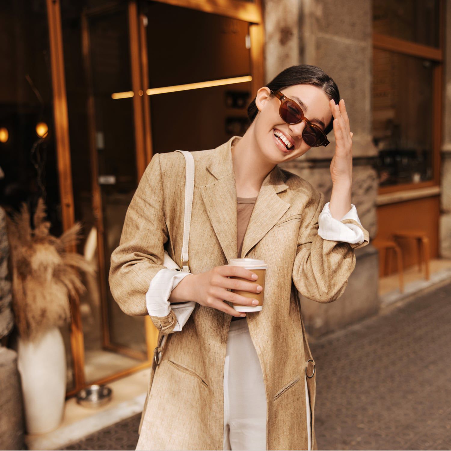 A woman walking down a city street with coffee and smiling.