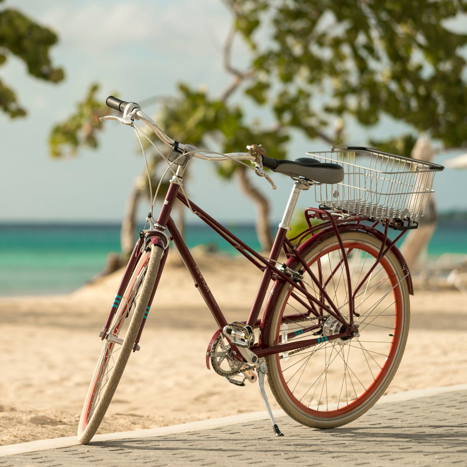 A bicycle with a rear basket on a sidewalk beside the beach.