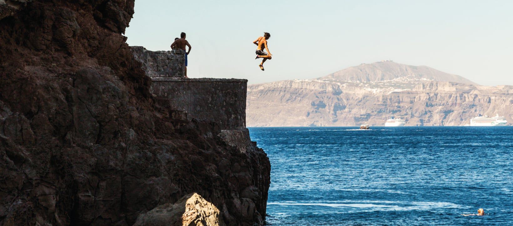 A group of boys cliff diving into the ocean below.
