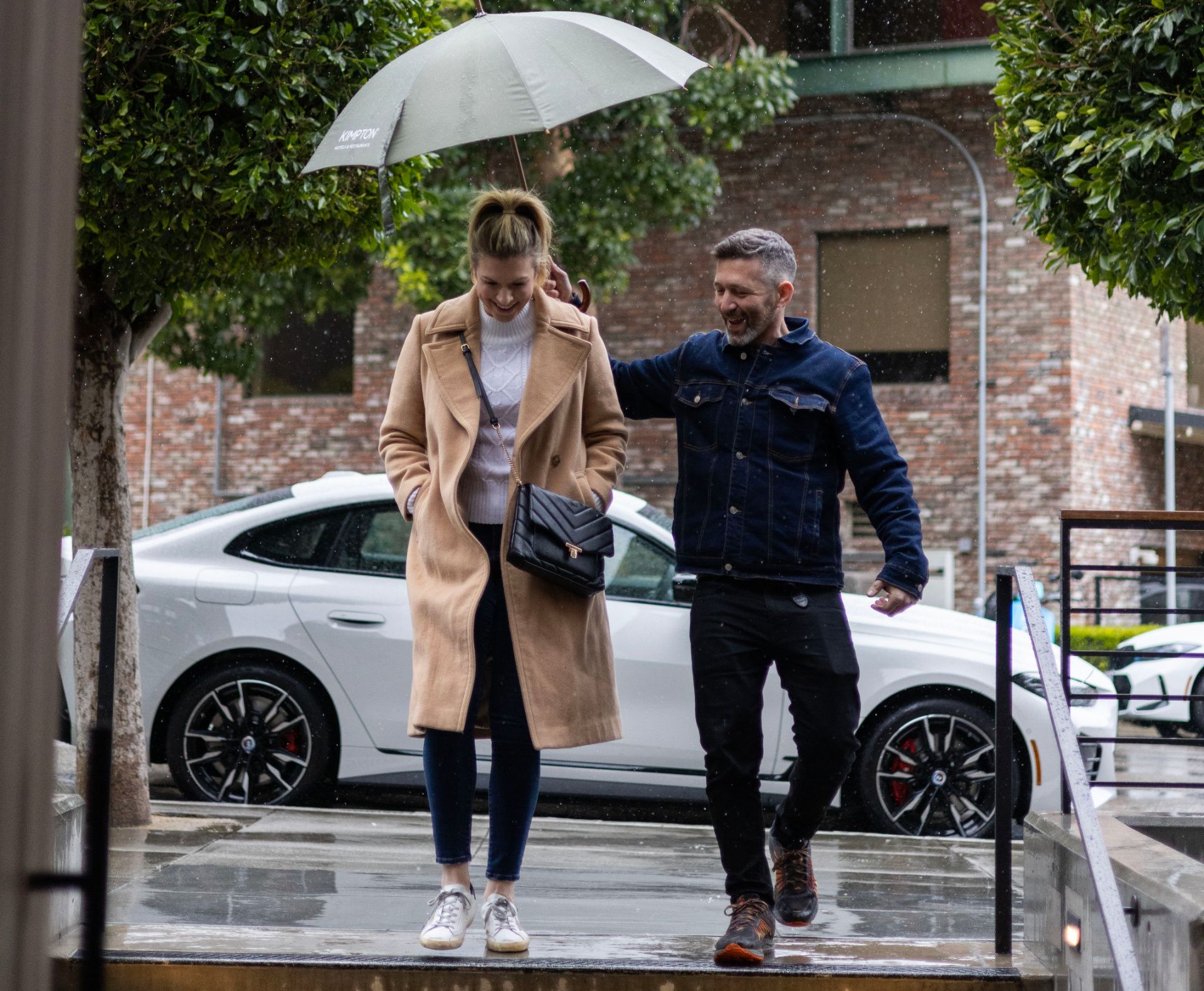 man holding an umbrella over a woman walking from car to hotel entrance