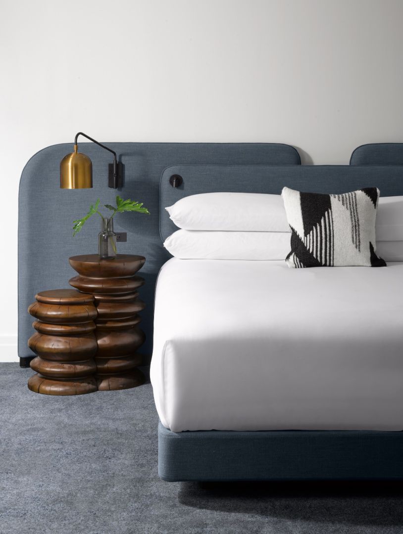 crisp white bed with rustic carved wood side tables and gray headboard