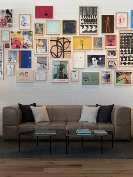 A wall full of frammed art with gray couch below it 
