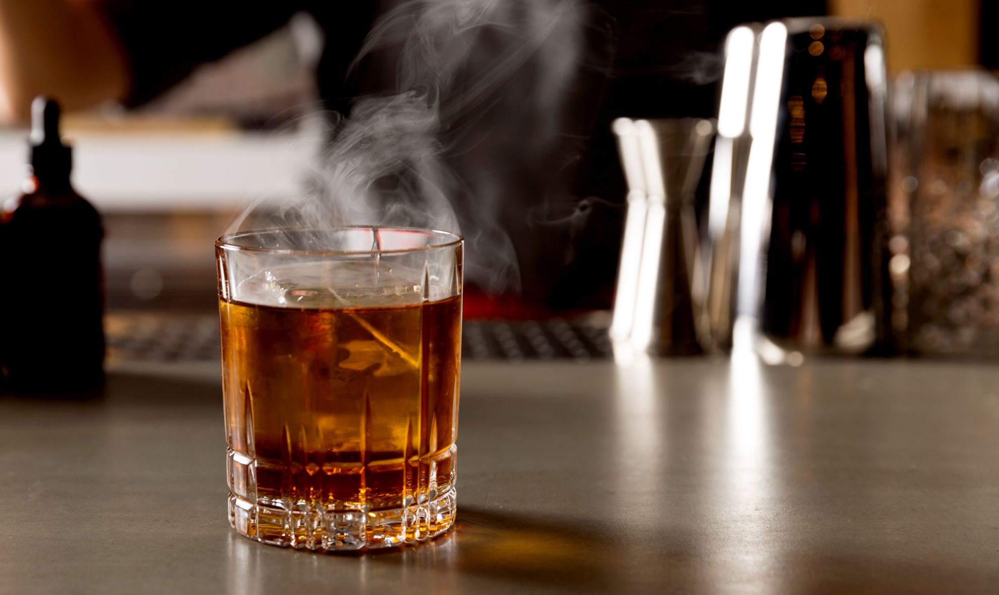 whiskey cocktail in cut glass smoking on the bartop