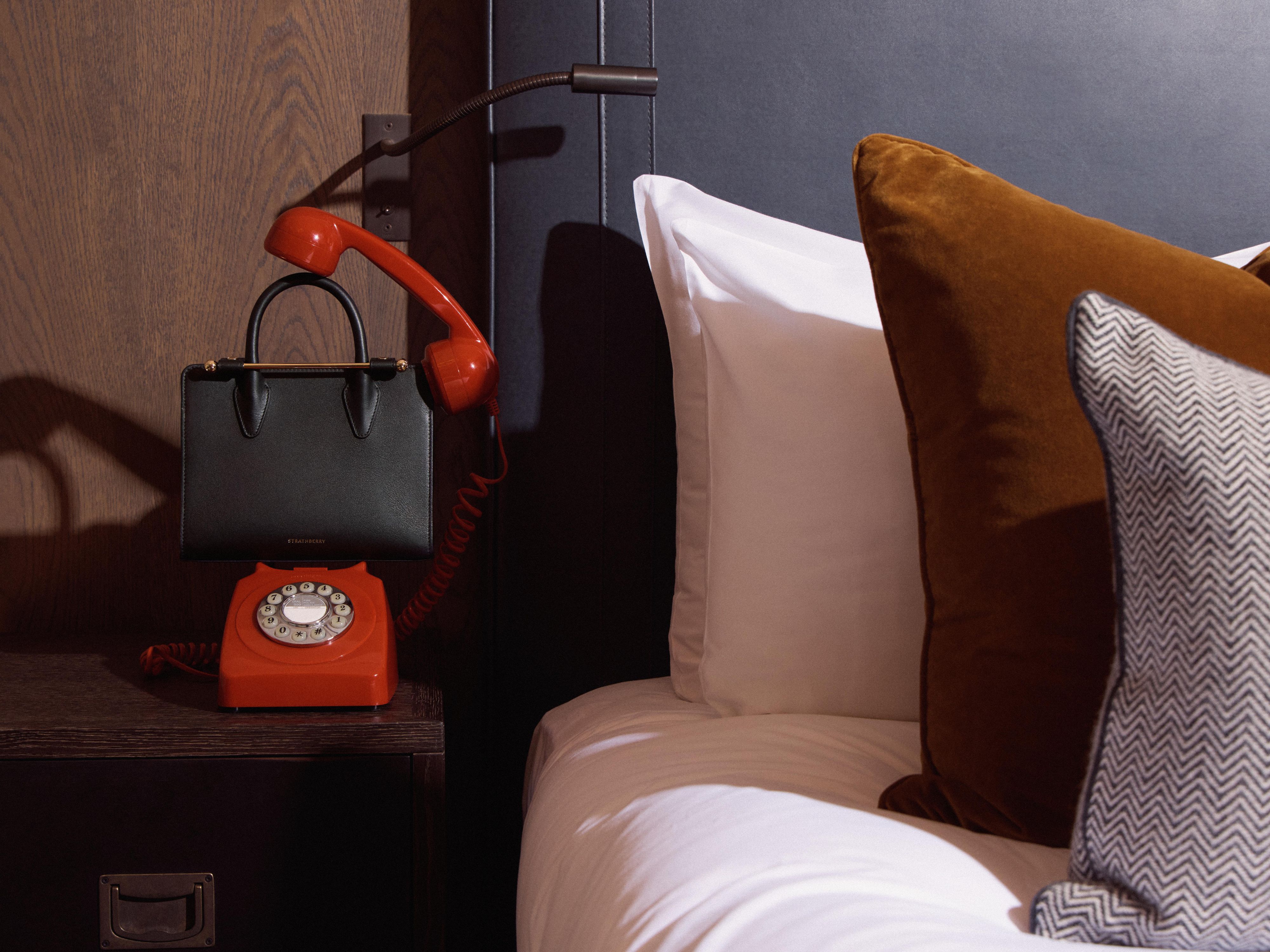 A stratehberry handbag in between a British red telephone on a luxury hotel guestroom bedside table