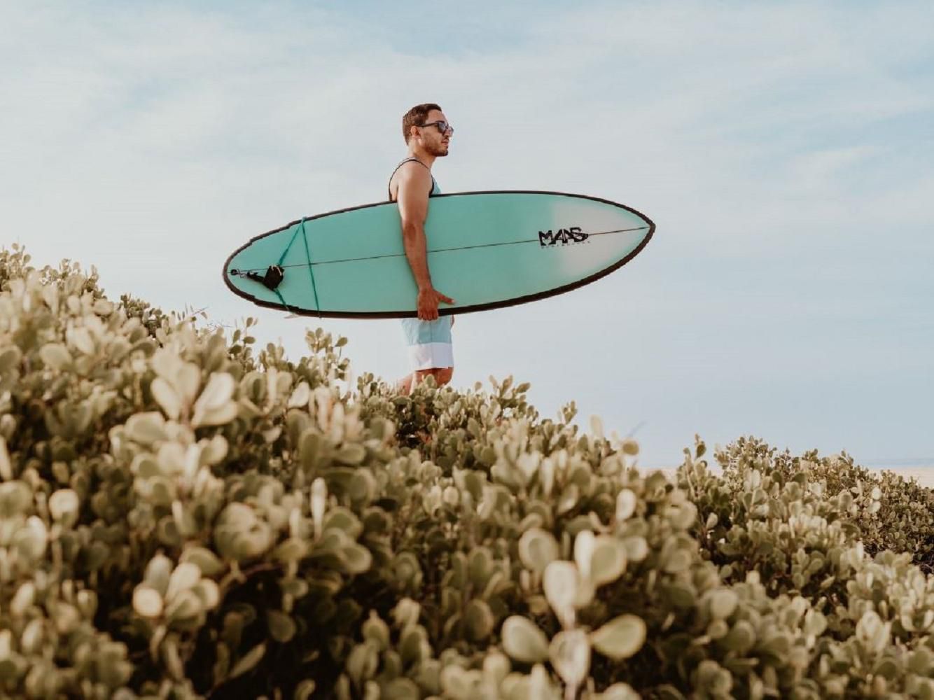Man standing on beach holding a surf board.