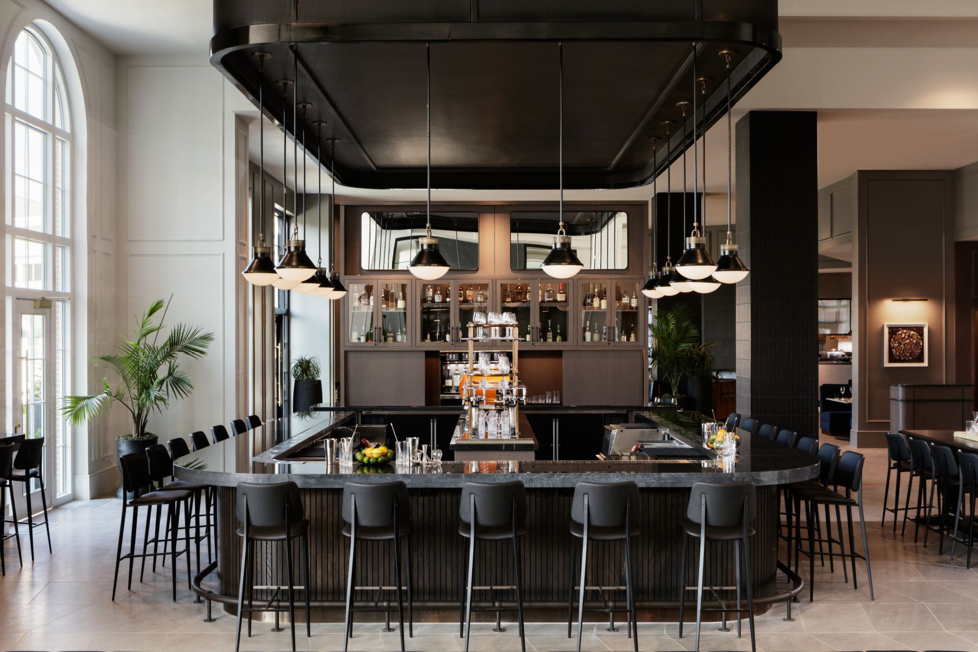 bar surrounded by restaurant seating with high ceilings and floor to ceiling windows