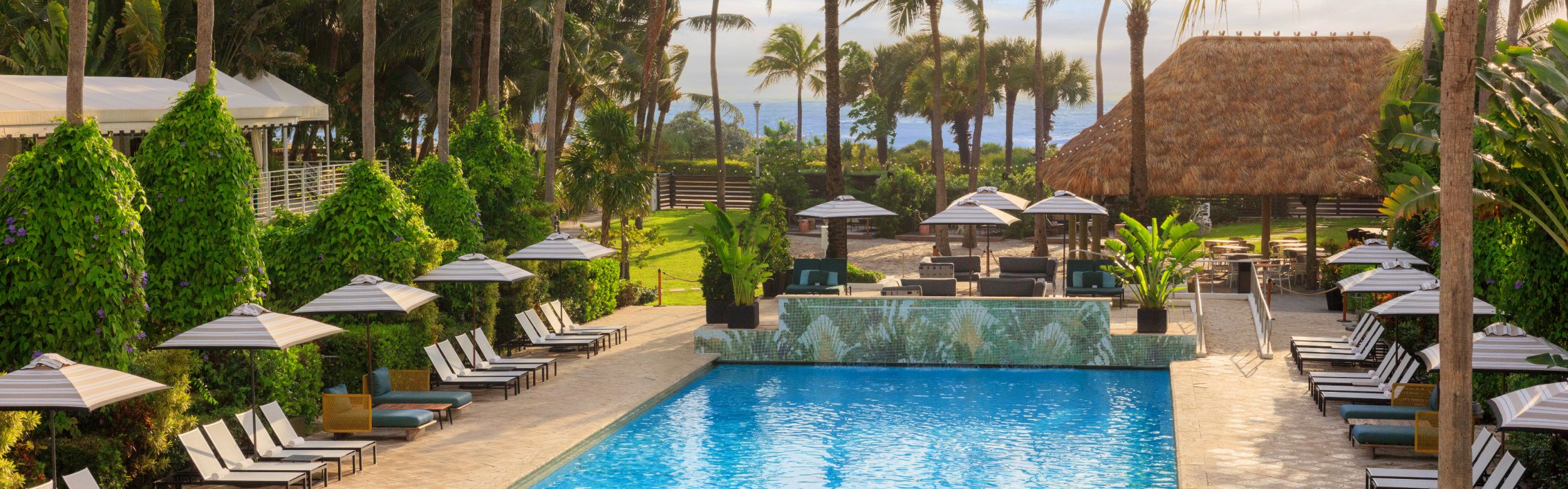 swimming pool surrounded by lounges, umbrellas with ocean views