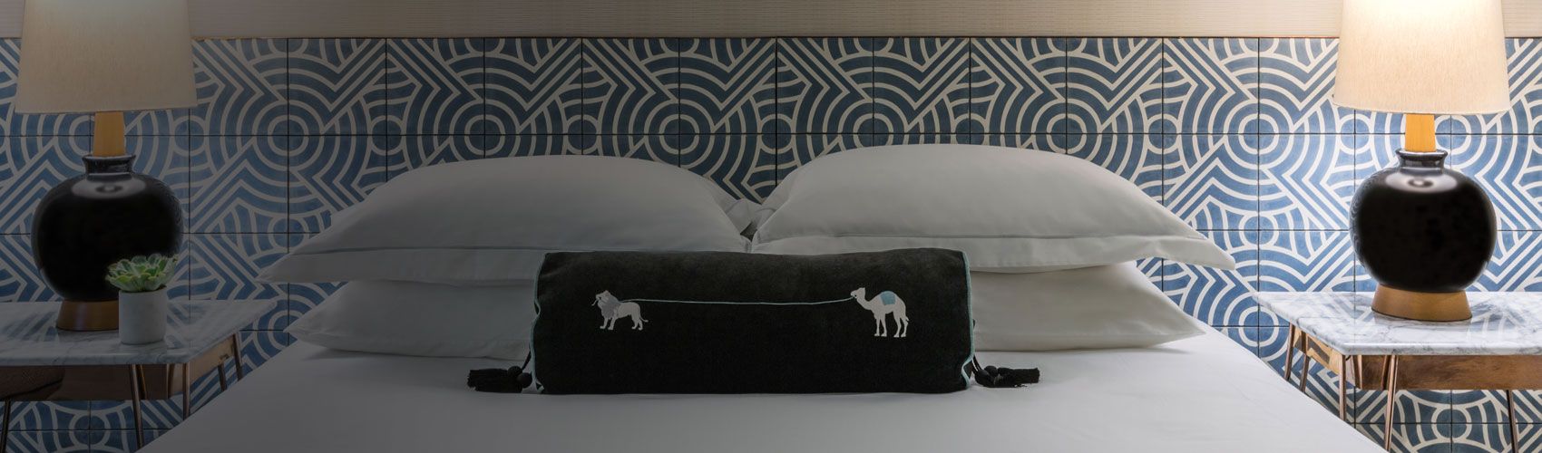 Hotel room view of queen bed with decorative pillow