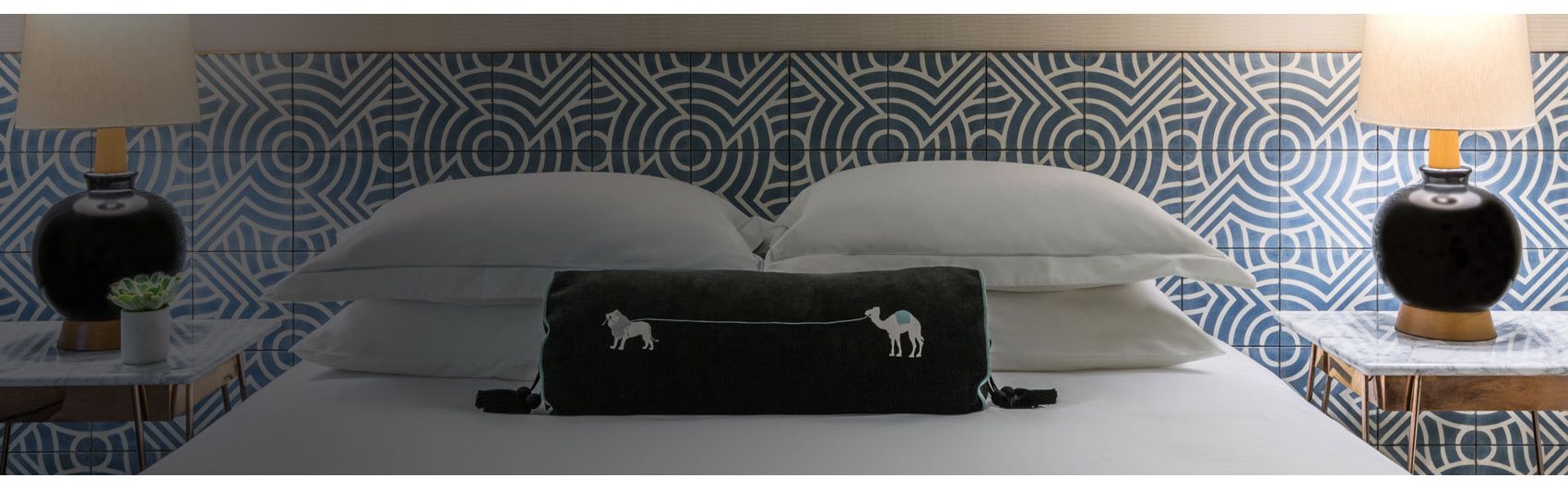 Hotel room view of queen bed with decorative pillow