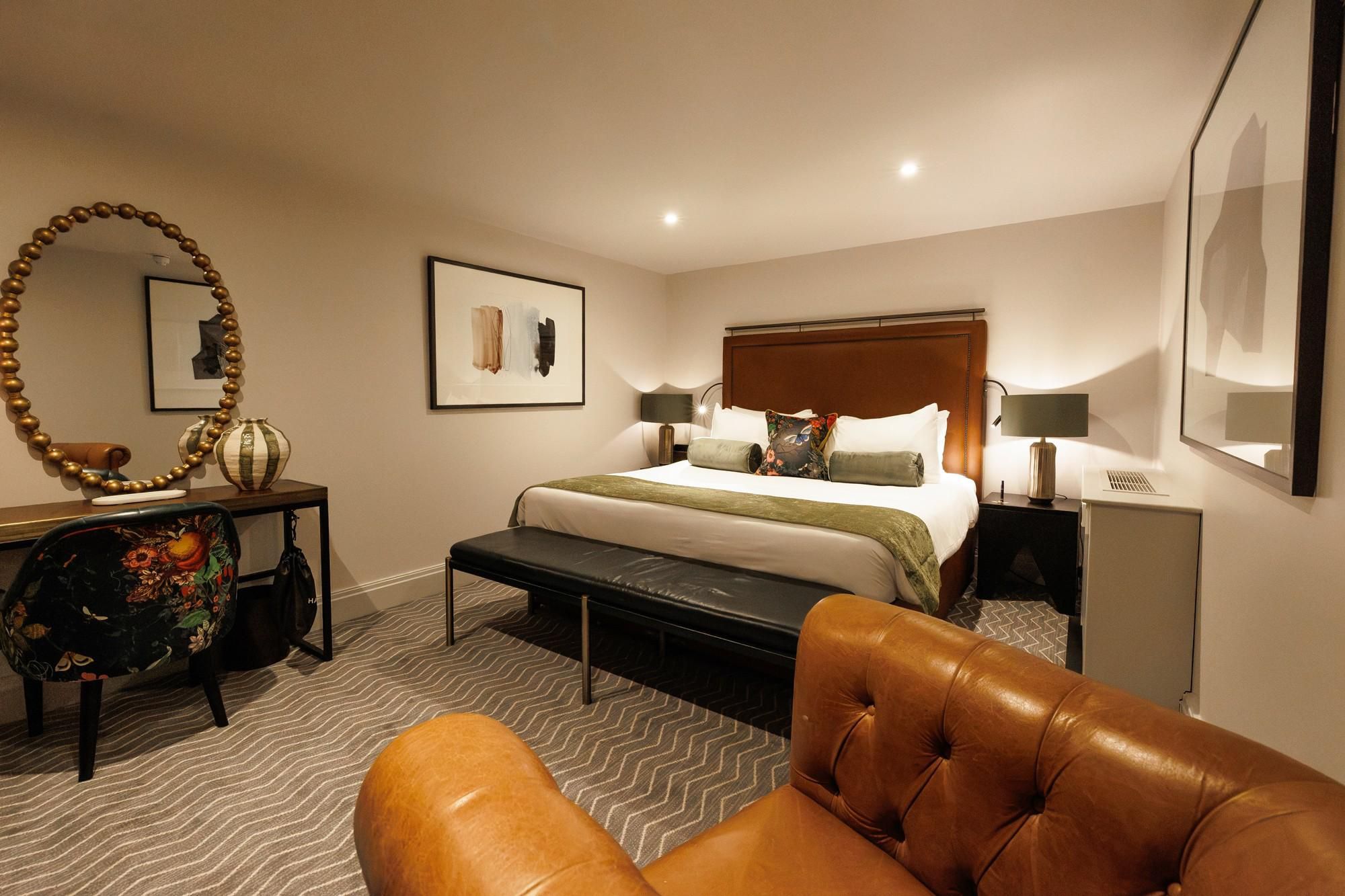 Deluxe king suite with bed, mirror and cosy armchair