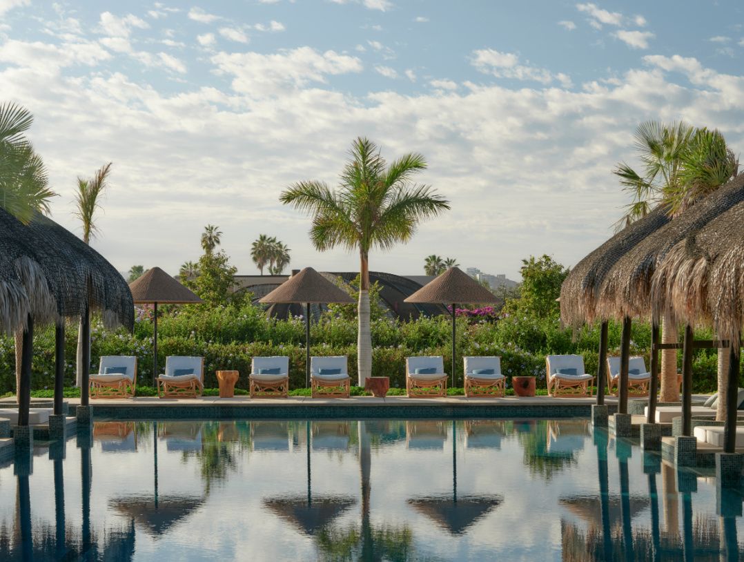 thatched umbrellas and palm trees surrounding a resort swimming pool