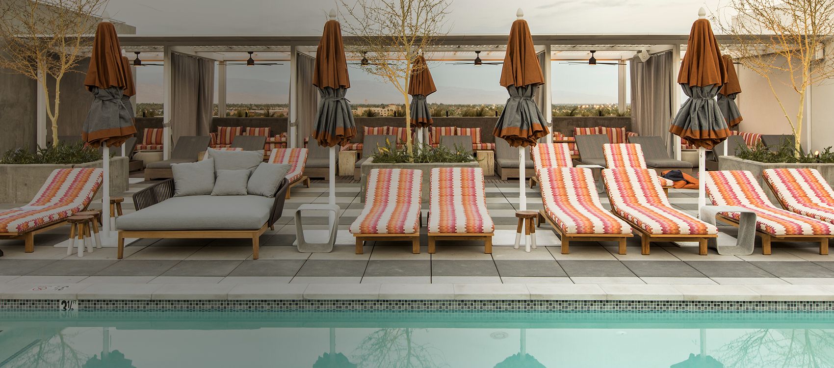 striped chaise lounges line a pool with views of desert mountains behind