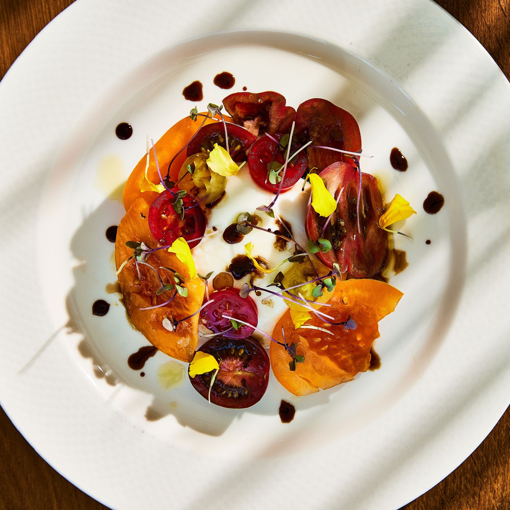 deeply colored sliced tomatoes around burrata on a white plate