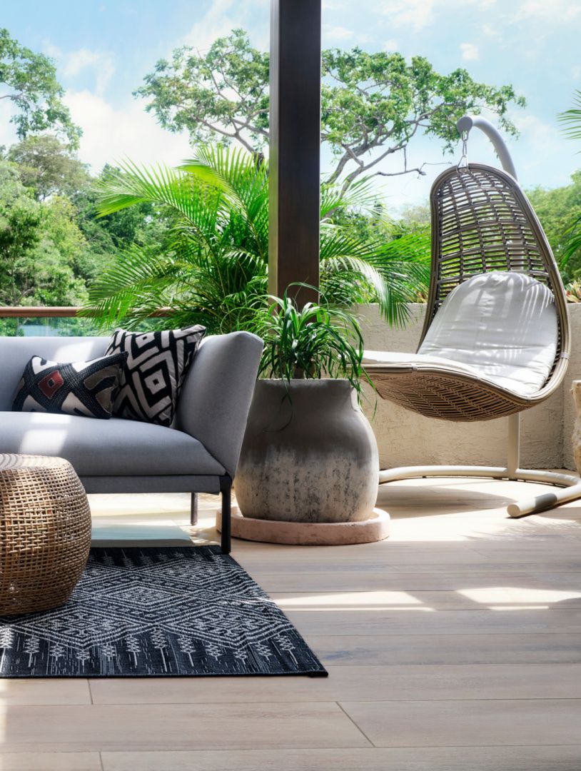 outdoor hanging seat and couch on a balcony with lush trees behind