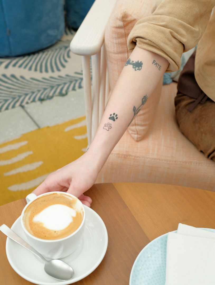một người phụ nữ với hình xăm nhỏ trên cánh tay của mình với cà phê