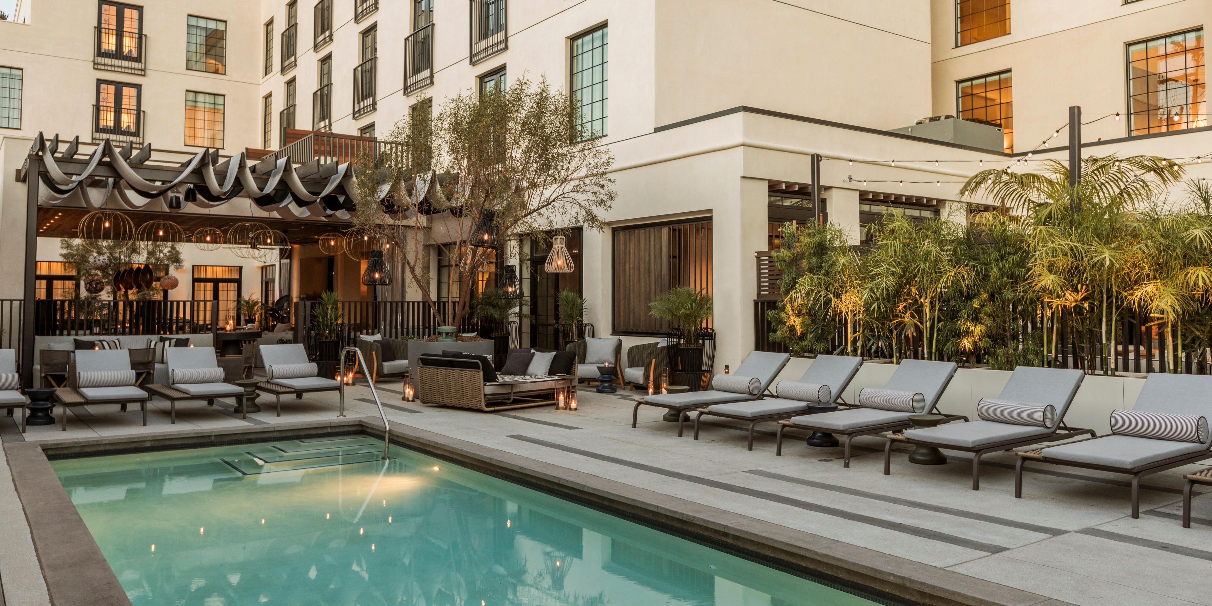The artistry of Kimpton La Peer Hotel extends to our open-air courtyard pool. Olive trees offer shade by day, the soft glow of hanging lanterns by night. A hand-sculptured wall and comfortable lounge chairs add to the tranquil scene.