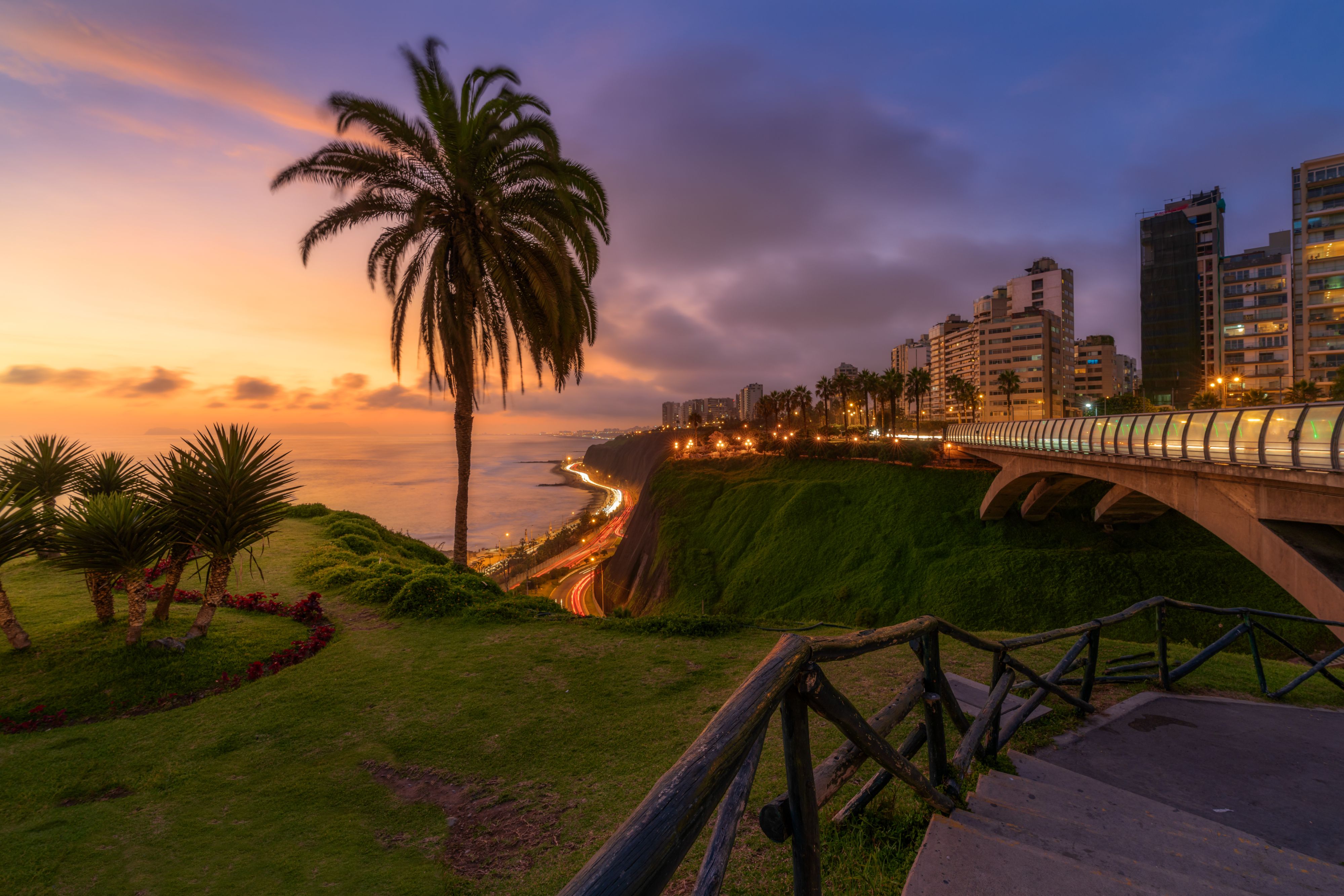 Puesta de sol sobre los acantilados costeros, las palmeras y el horizonte frente al mar de Lima.