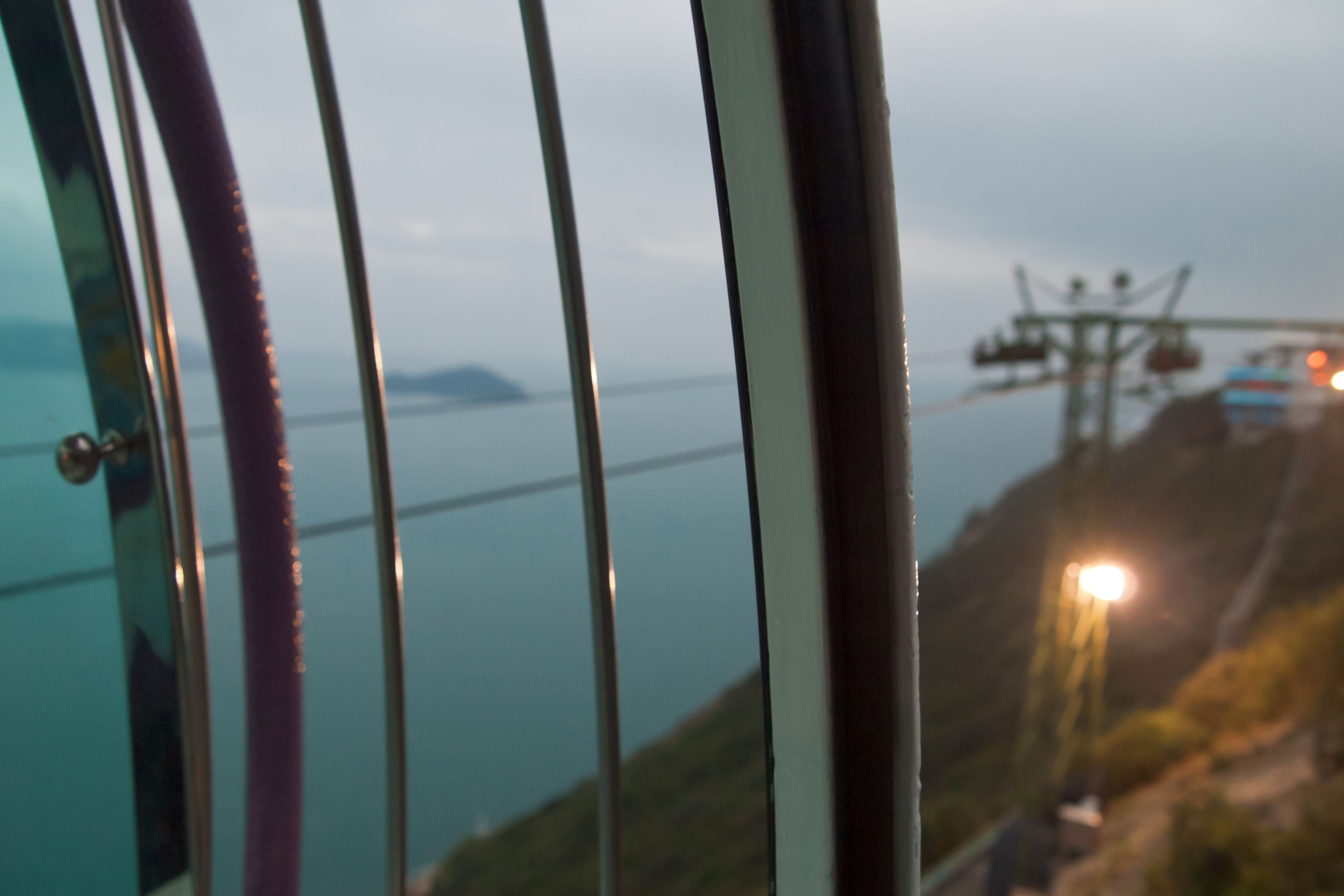 View from a cable car overlooking a coastal hillside and calm water.
