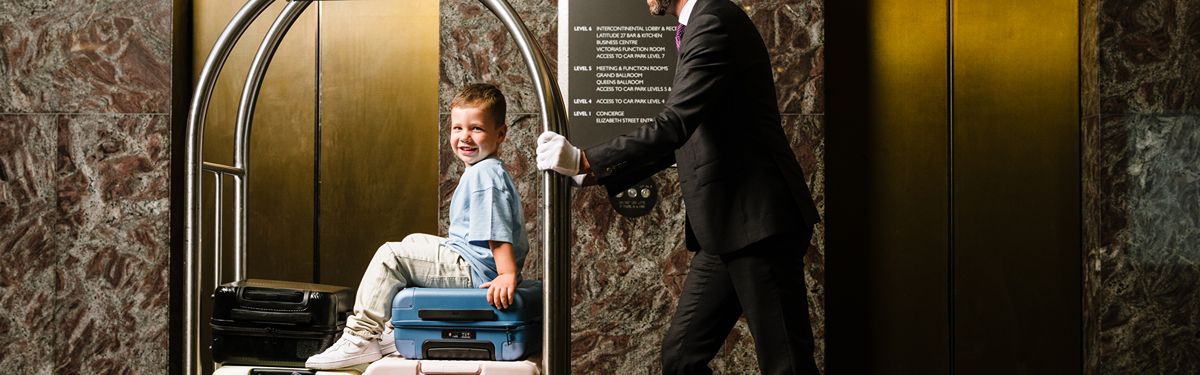 Child seated on a luggage trolley during a Little Luxuries family stay at InterContinental Brisbane. 