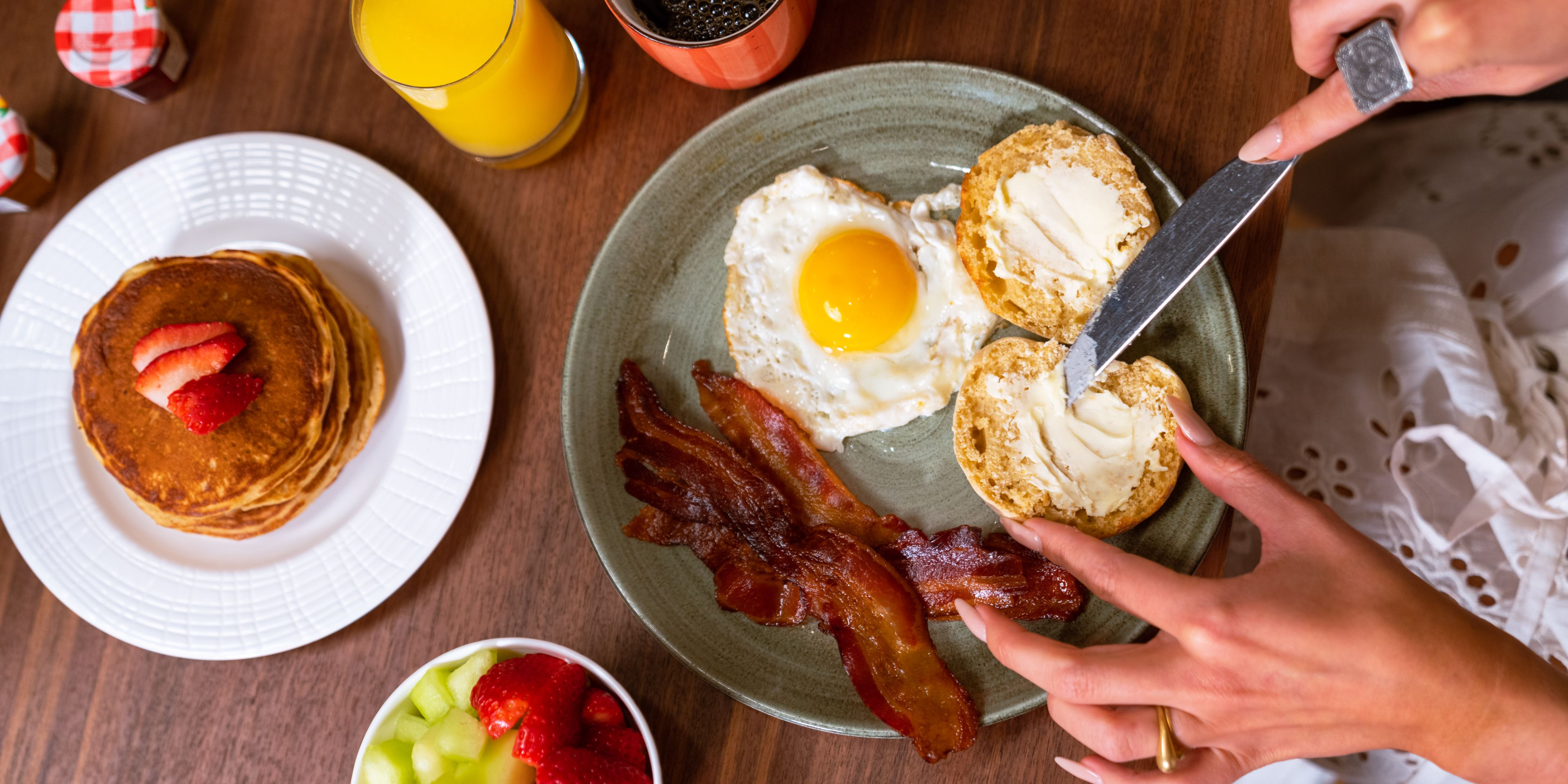 Guest butter english muffin on their breakfast plate, including eggs and bacons and a side fo pancakes.