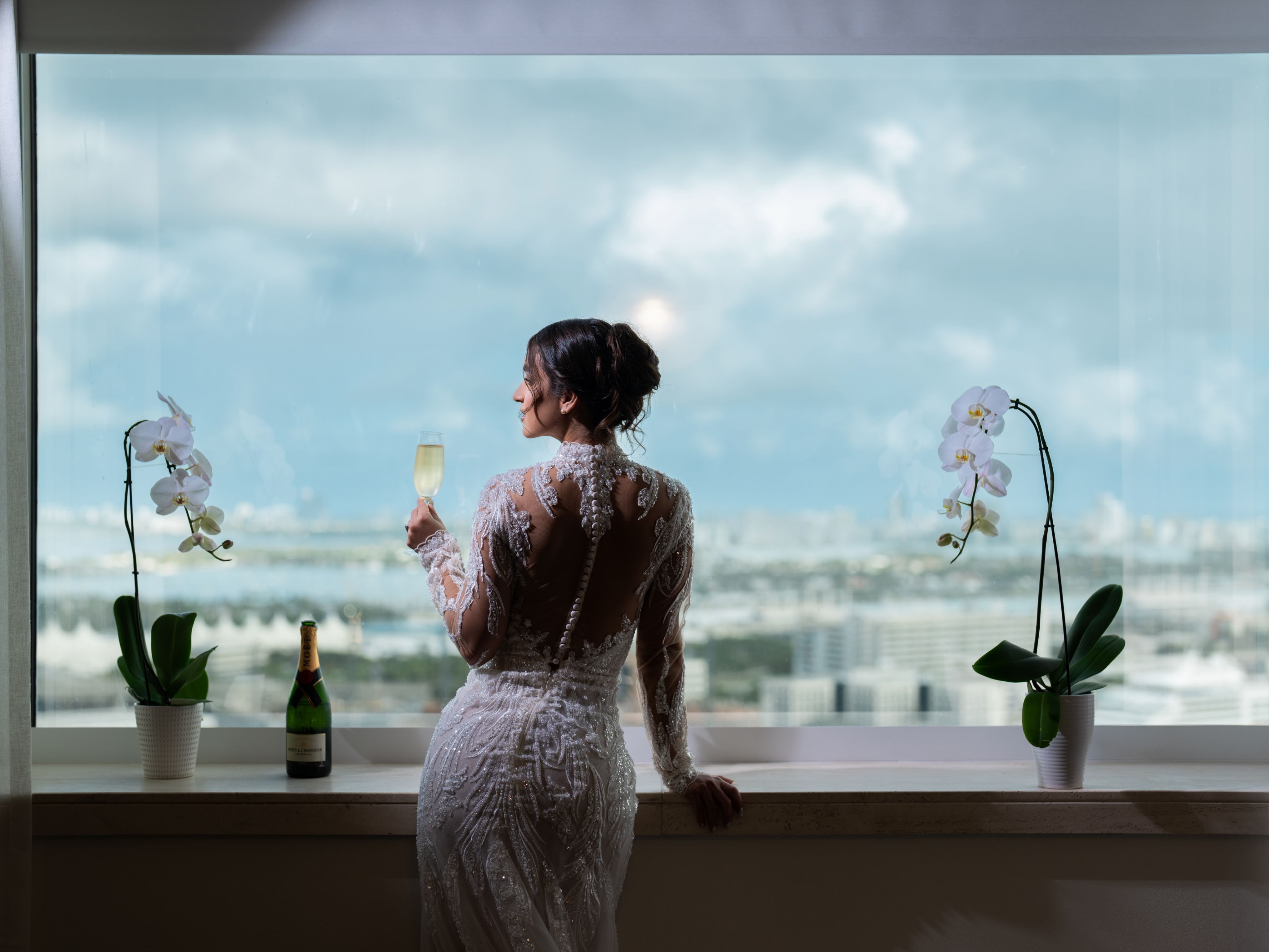 Bride standing by the window in a suite with champagne.