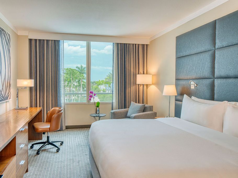 Modern guest room with a king bed, work desk, lounge chair, floor-to-ceiling window, and views of palm trees at InterContinental at Doral Miami.