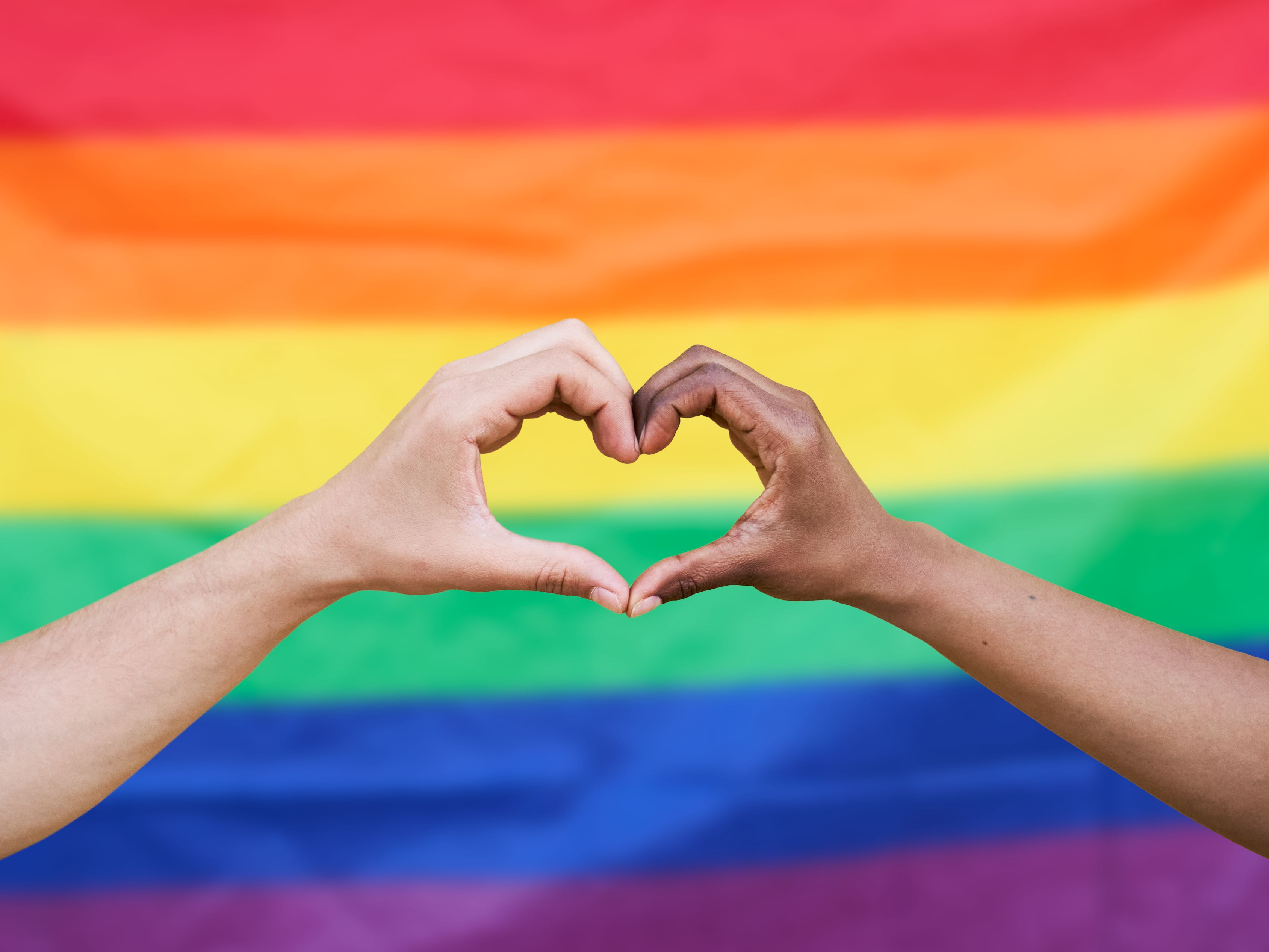 hands making a heart shape in front of pride flag