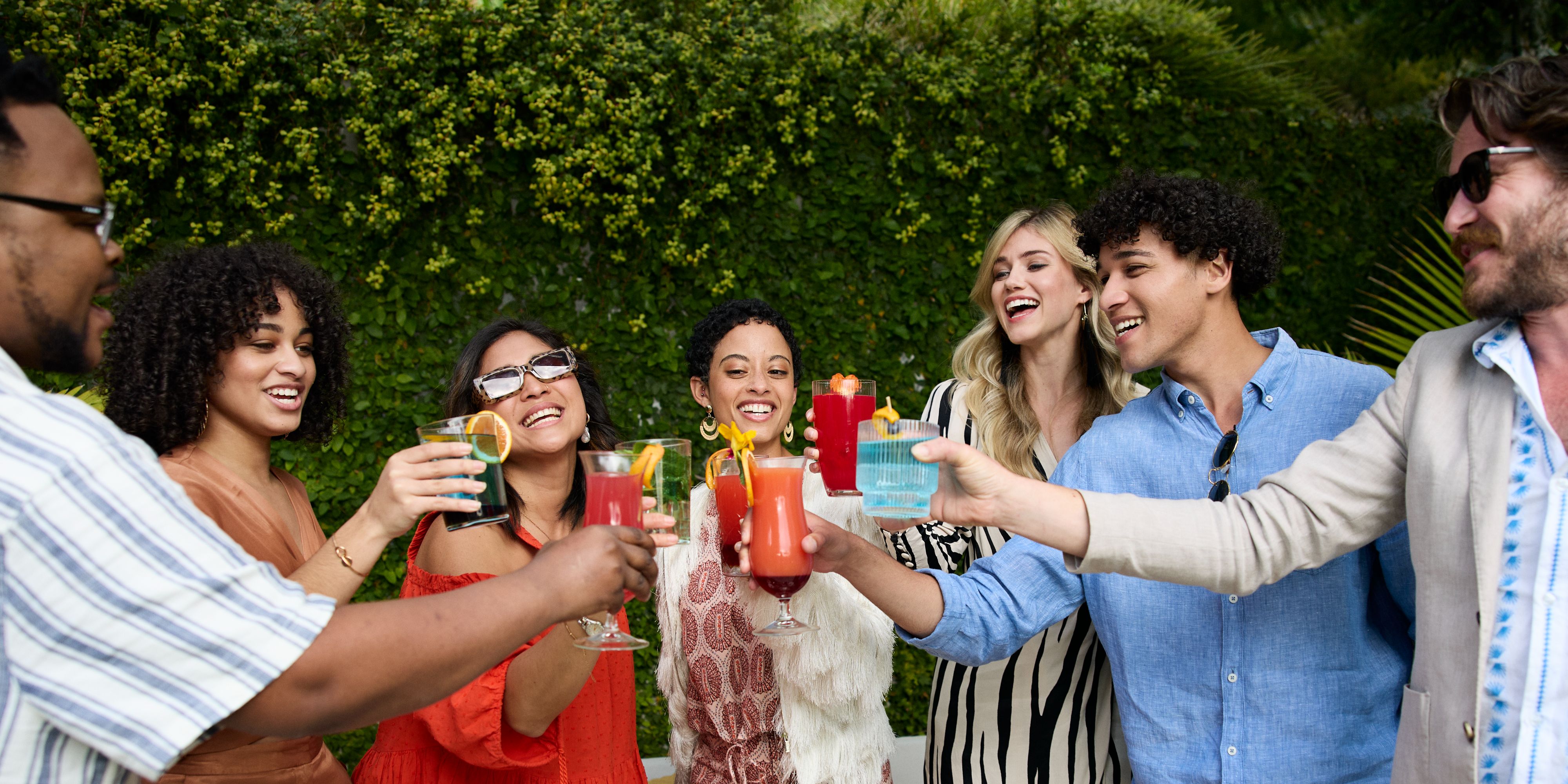 Friends raising colorful cocktails in Bossa House's lush garden setting.