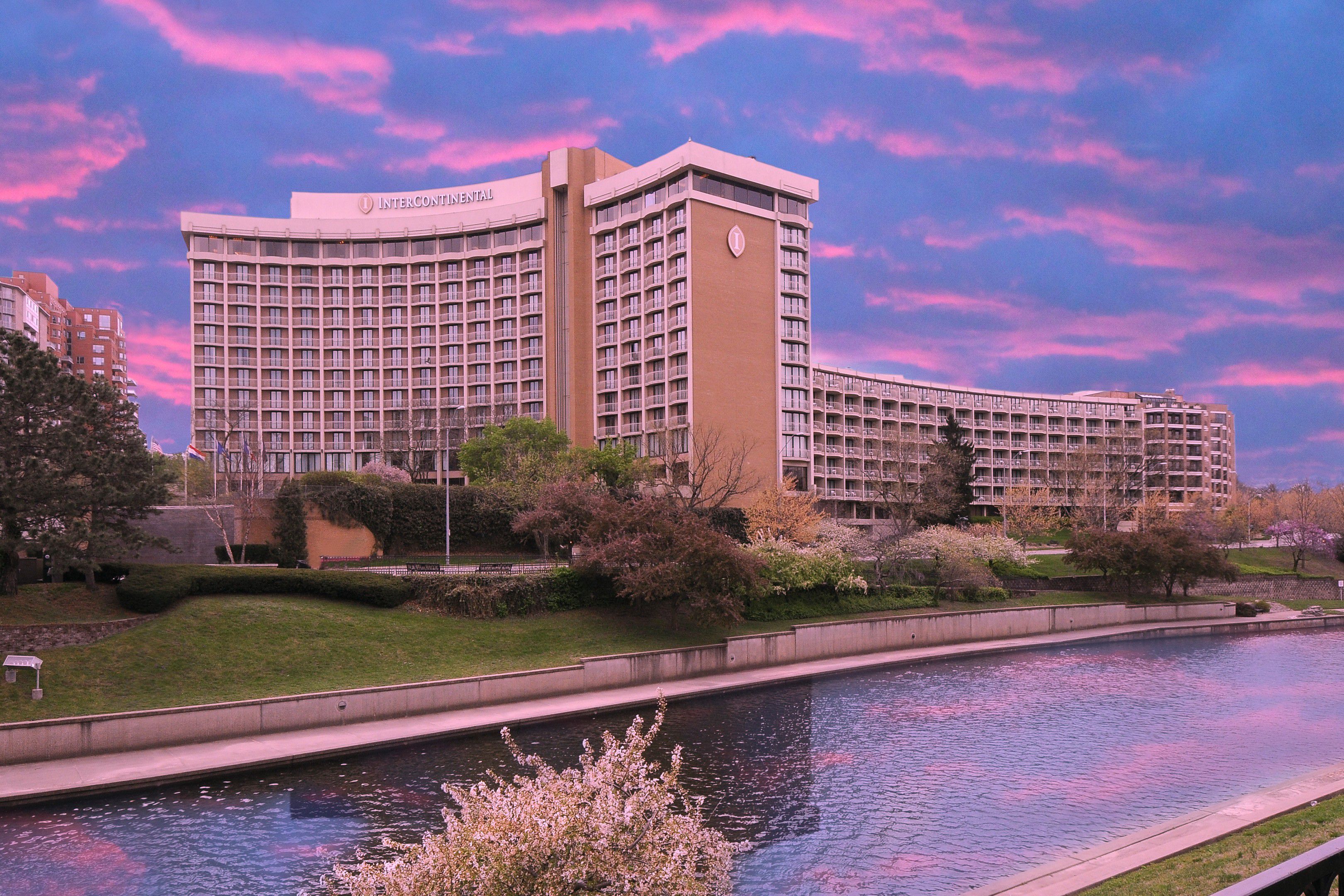 Exterior view of InterContinental Kansas City at the Plaza beside a river at sunset with pink and blue sky.
