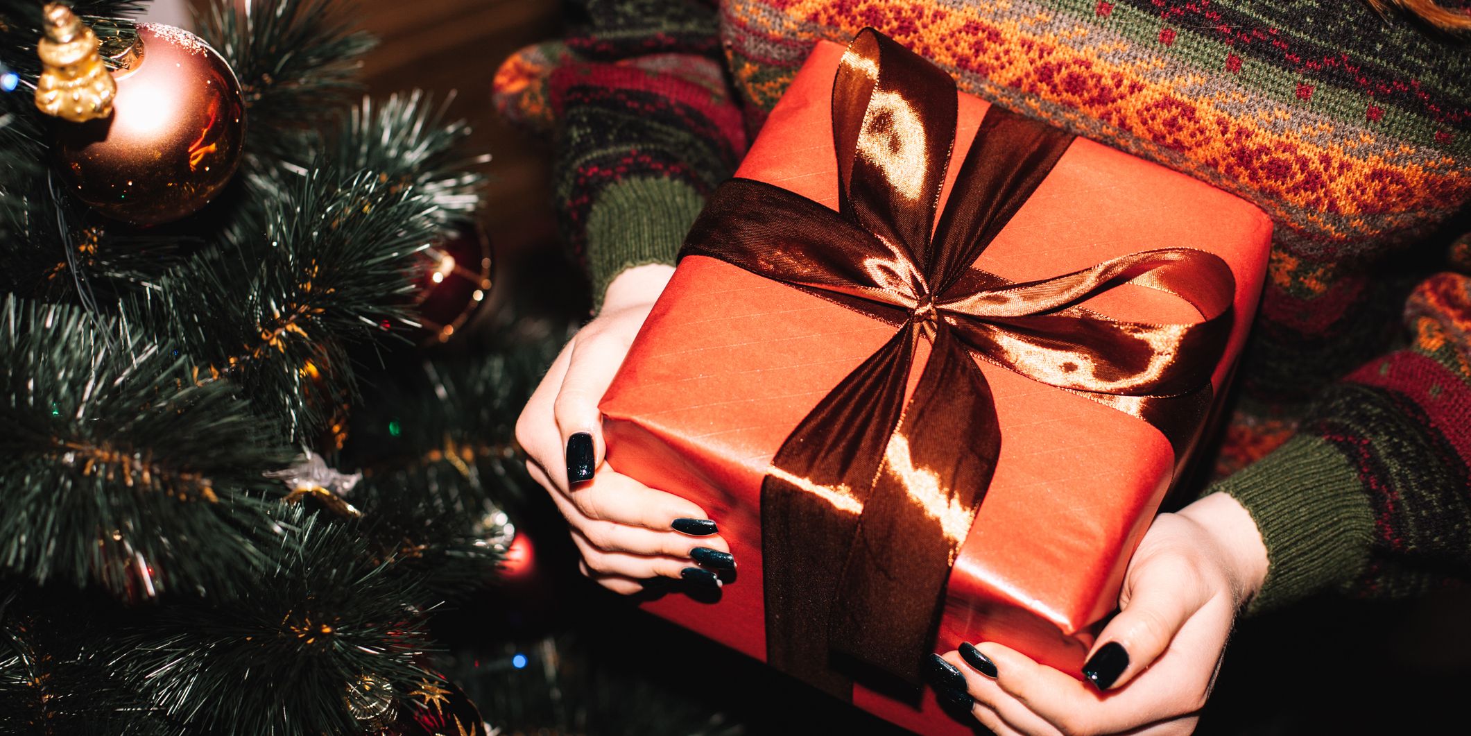 woman holding christmas present in front of tree