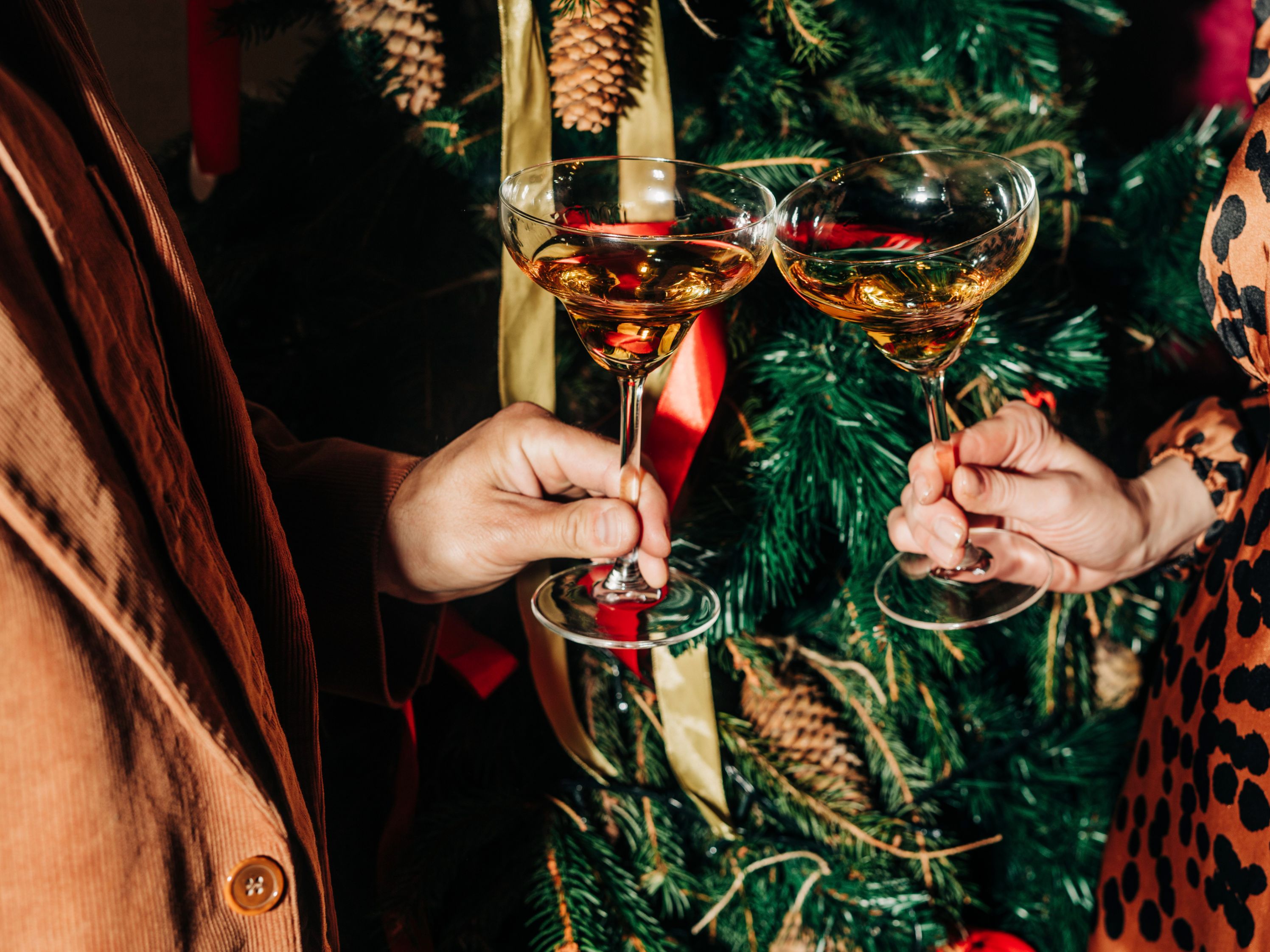 two people holding cocktails in front of Christmas tree