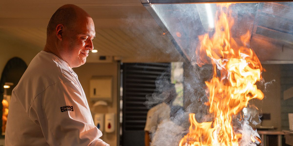 Chef preparing food over an open kitchen flame.