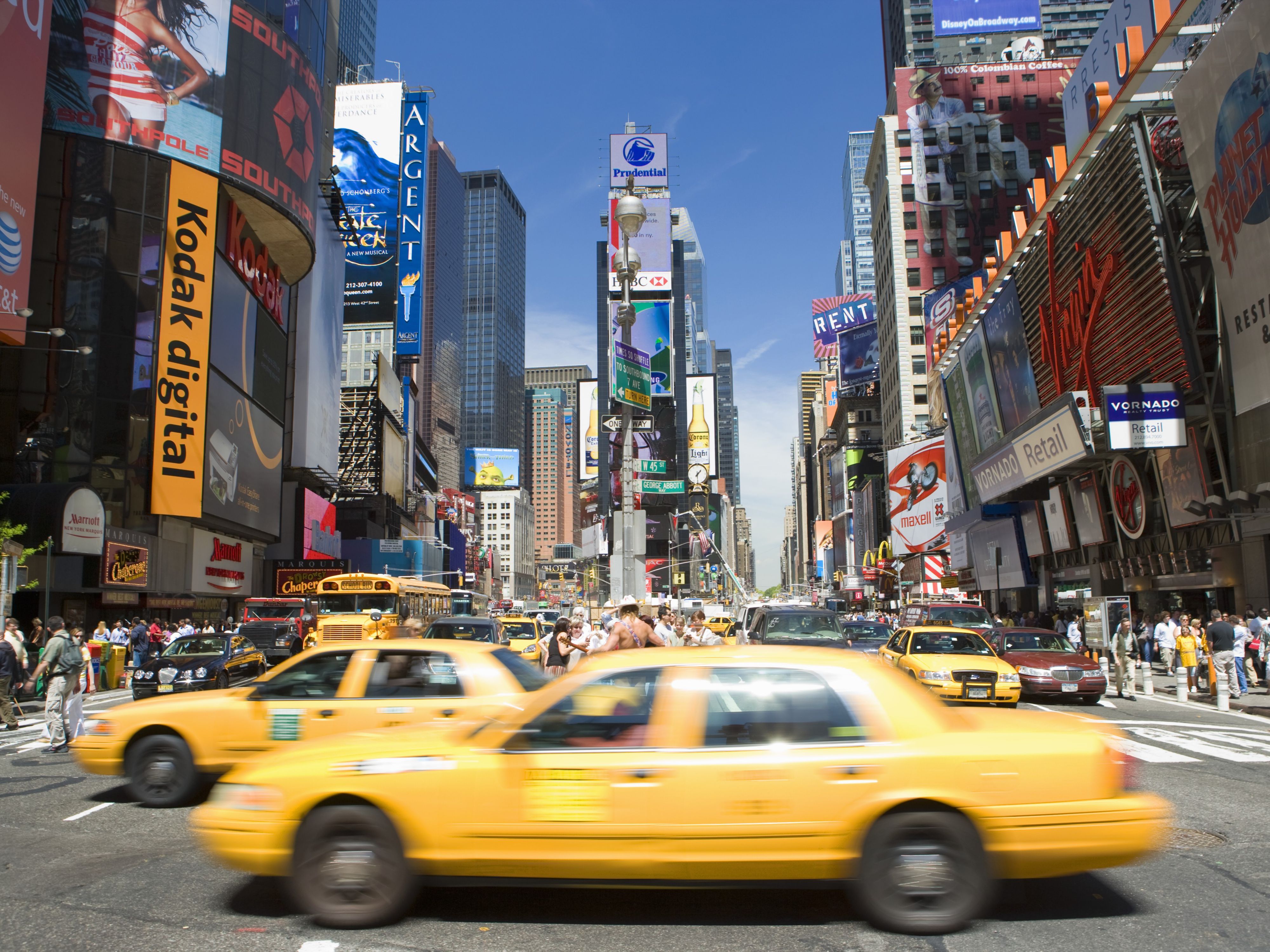 Cabs driving by Times Square during the day.