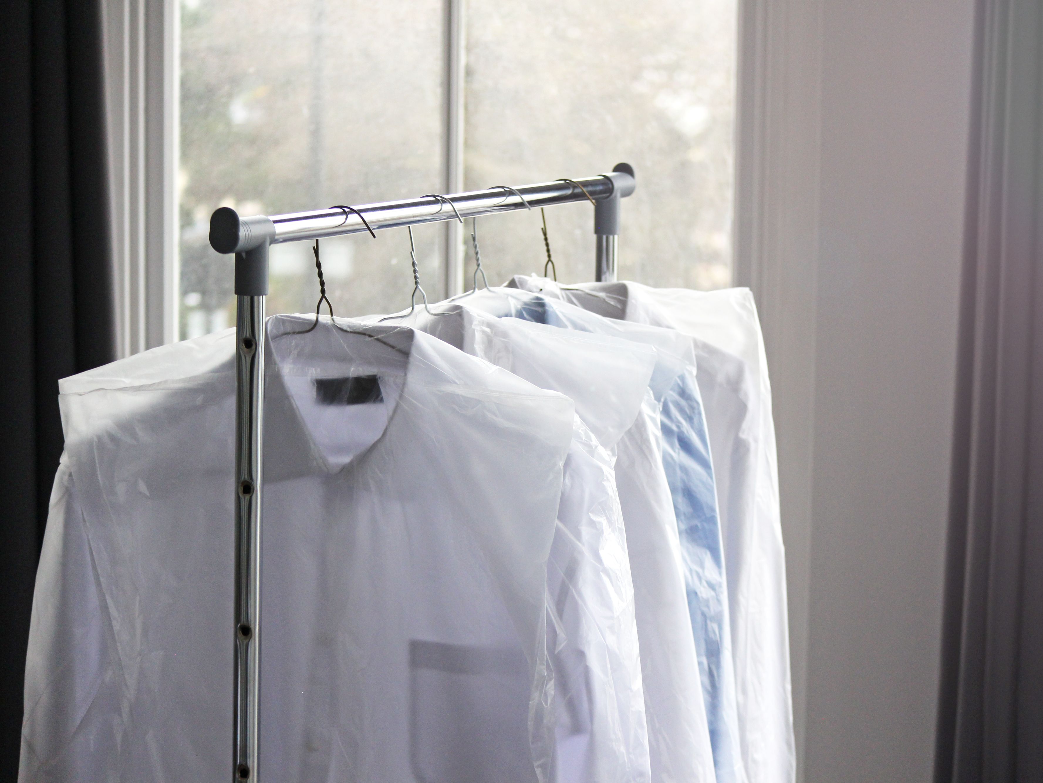 clothes in dry cleaning bags hanging on a rack
