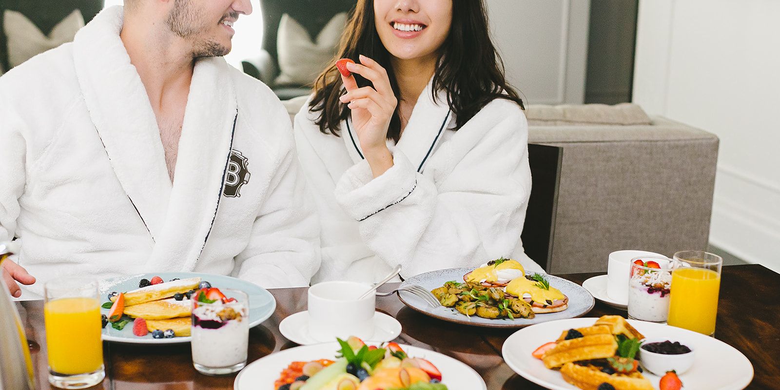 Couple enjoying our in room dining breakfast with waffles, pancakes, fruit, eggs benedict, and sides.